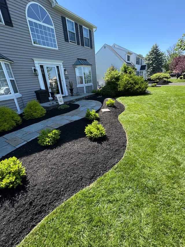 Curved front-yard mulch bed with boxwoods and low shrubs framing a stone walkway and porch.